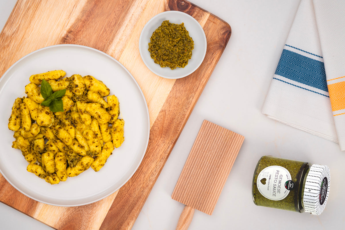 Green pesto sauce in white bowl on wooden board with coated potatoes on plate and jar with label.