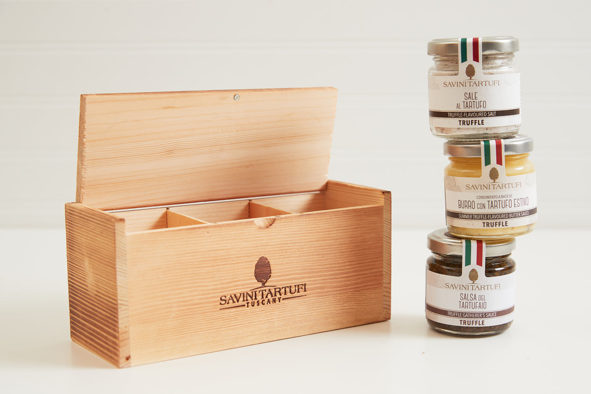 Wooden Savini Tartufi gift box with lid open beside three stacked glass jars of truffle products with Italian flag labels.