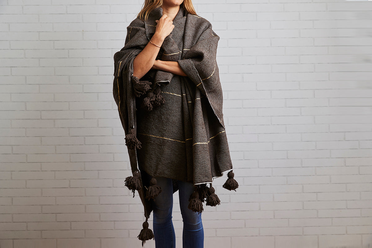 Charcoal wool blanket with gold stripes and black tassels draped around woman's shoulders.