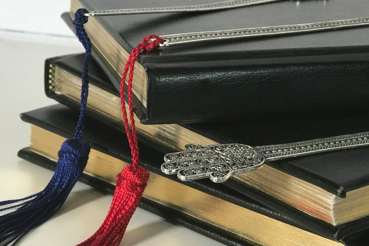 Silver Hand of Fatima bookmark with navy and red tassel cords displayed on stacked books.