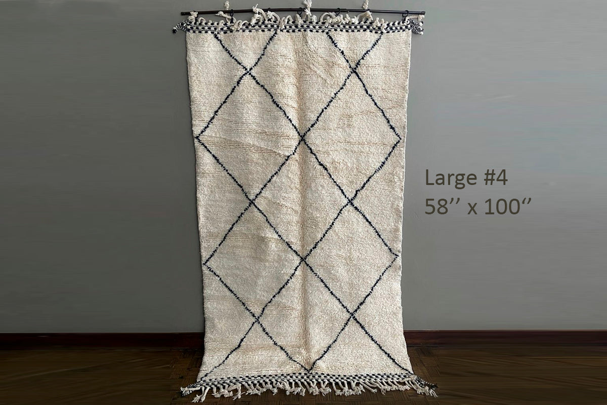 Cream-colored Berber rug with black diamond pattern and fringe edges, displayed hanging from rod.