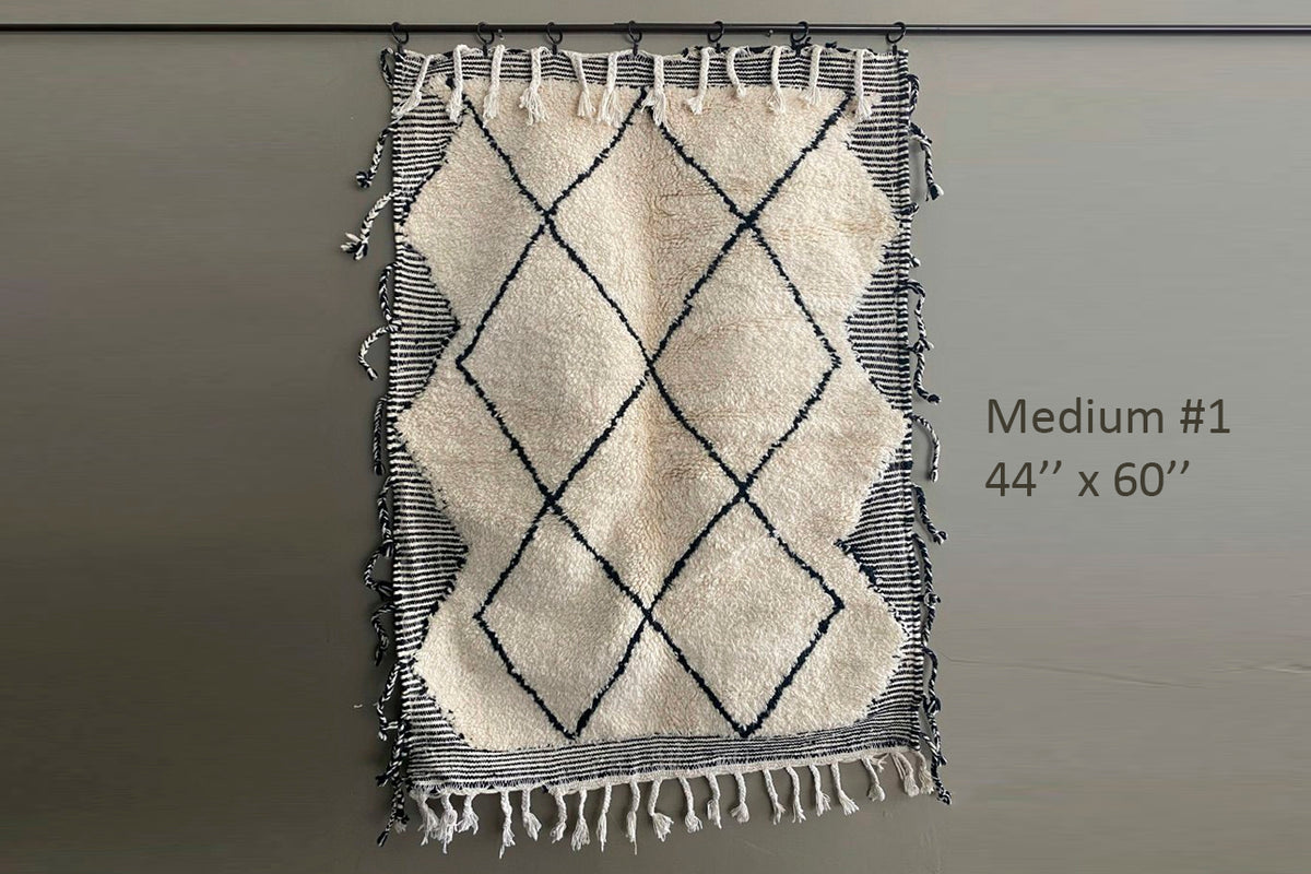 Cream wool rug with black diamond pattern and striped borders, displaying traditional Berber design with fringe edges.