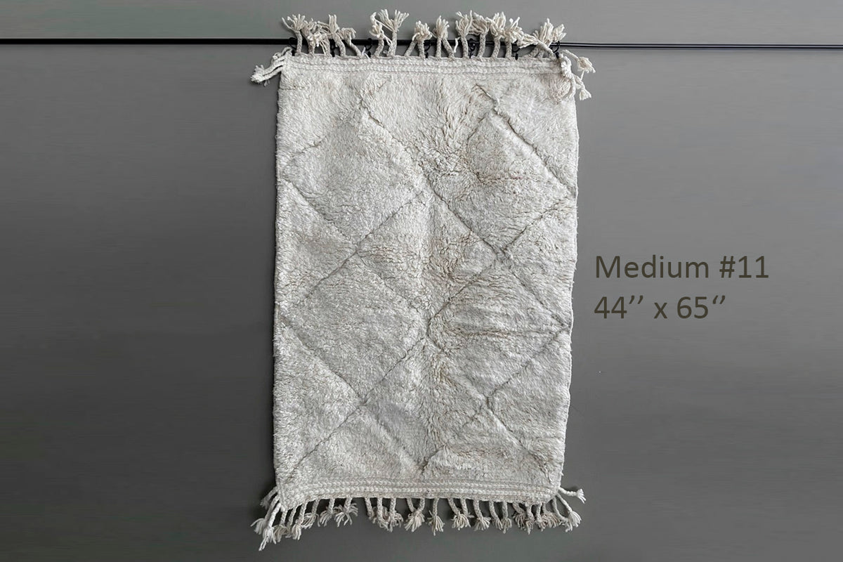 Cream-colored wool rug with diamond pattern and knotted fringe edges, 44" x 65".