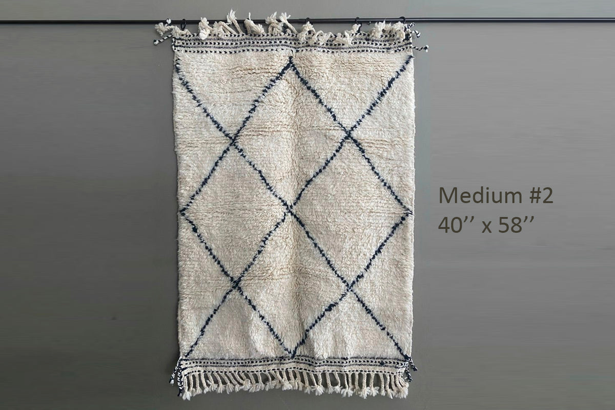 Cream-colored handwoven rug with navy diamond pattern and fringe trim, 40" x 58".