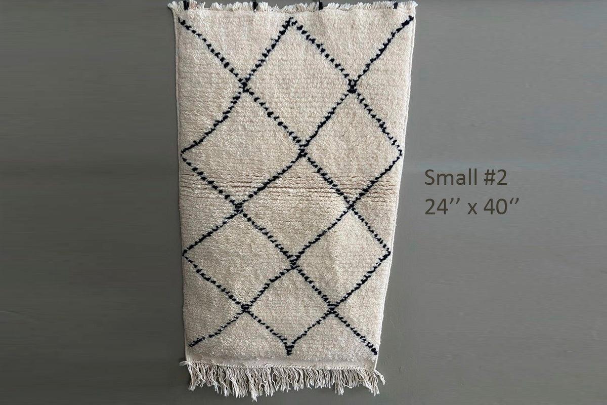 Cream wool rug with black diamond pattern and fringe trim, 24" x 40".