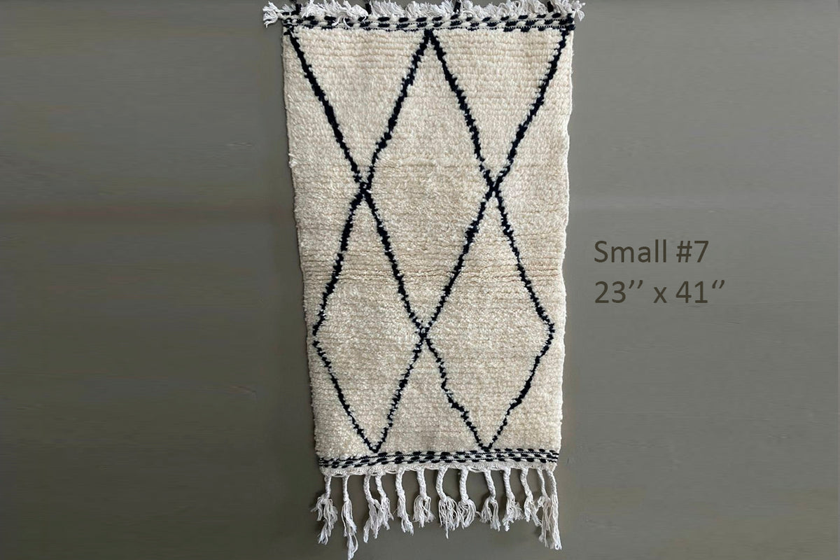 Cream-colored Berber rug with black diamond pattern and fringe ends, 23" x 41".