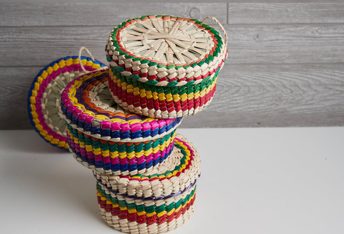 Stacked woven palm baskets with colorful fabric trim in red, green, blue, yellow, and pink stripes.