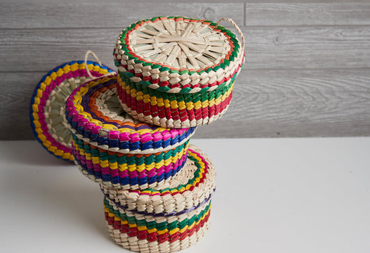 Stacked woven palm baskets with colorful fabric trim in red, green, blue, yellow, and pink stripes.