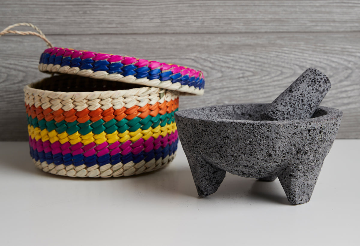 Gray stone molcajete with pestle and multicolored woven straw basket with handle.