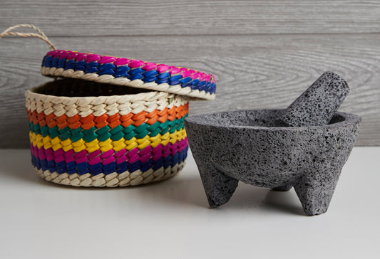 Gray stone molcajete with pestle and multicolored woven straw basket with handle.