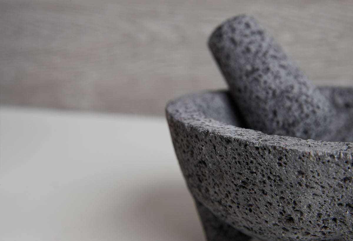 Stone molcajete with pestle, textured gray volcanic rock surface.