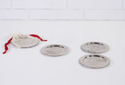Four round silver coasters with etched geometric patterns and metal rims, one with red fabric drawstring bag.