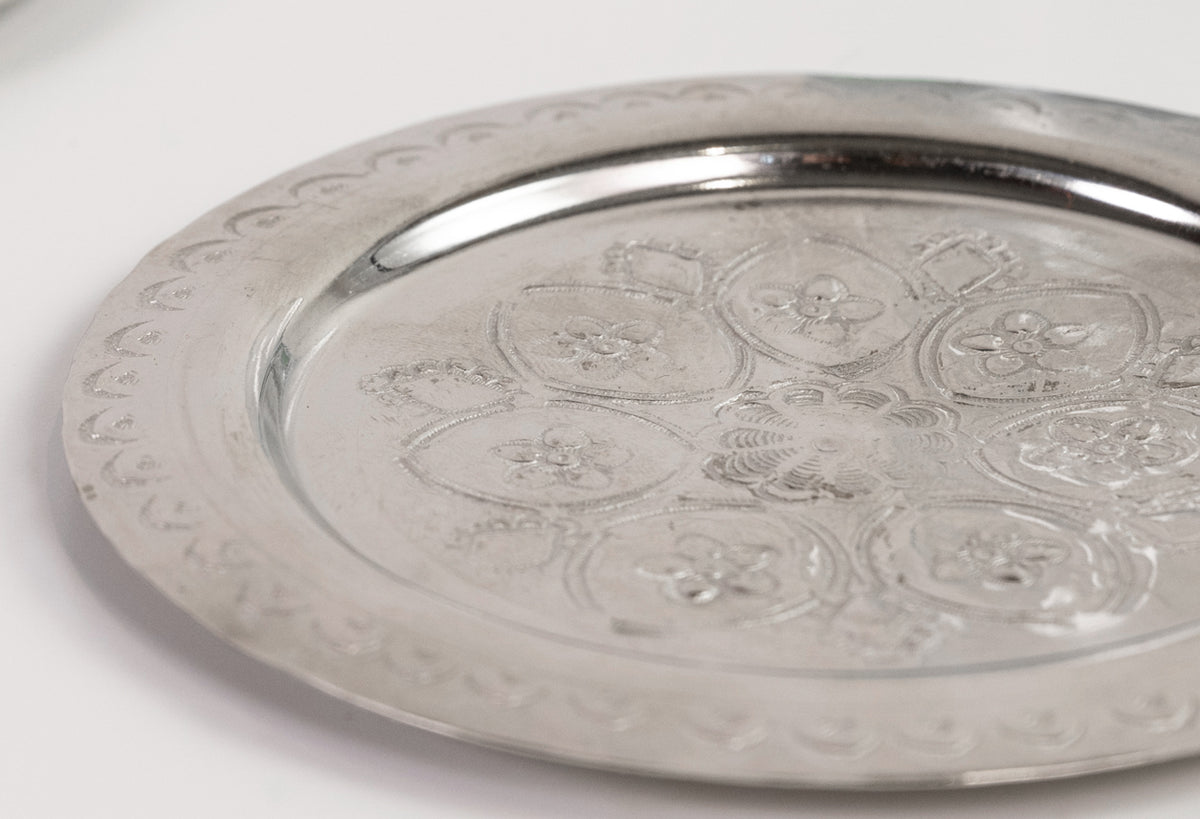 Silver coaster with embossed geometric and floral medallion patterns around the surface.