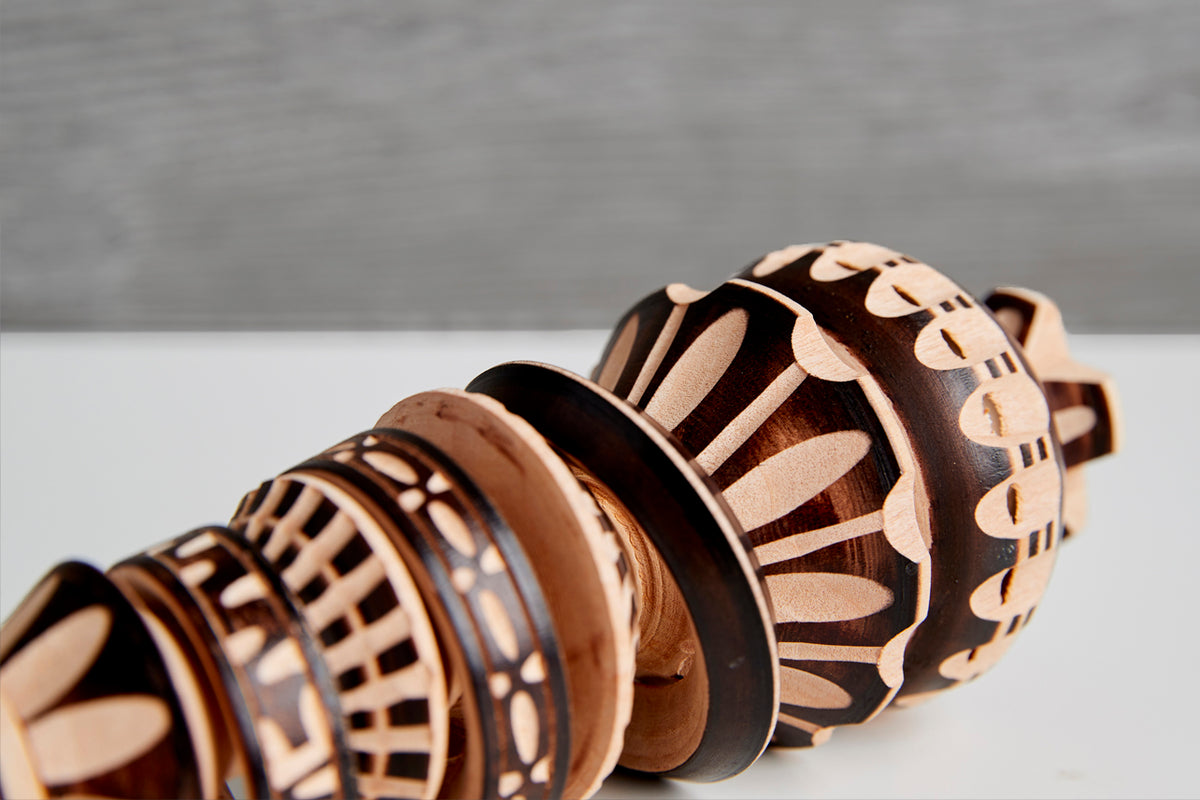 Wooden molinillo whisk with carved decorative bands and perforated spherical head, displayed at an angle.