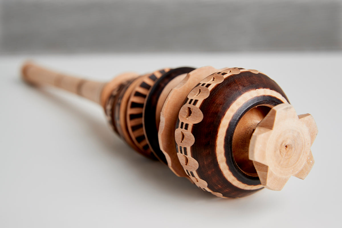 Wooden molinillo whisk with carved decorative rings and a bulbous head featuring carved paddle-like blades.