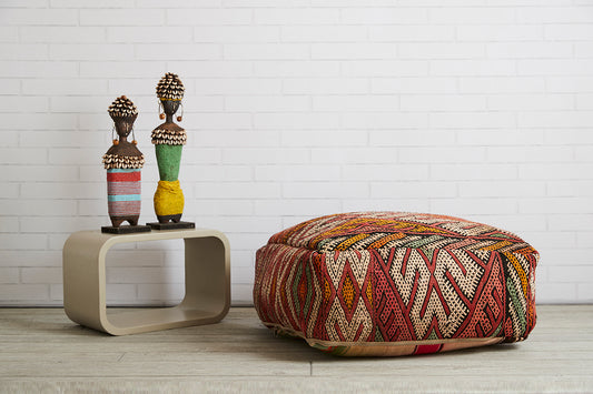 Woven kilim poufs with geometric patterns in red, rust, and cream tones, displayed on light wood flooring.