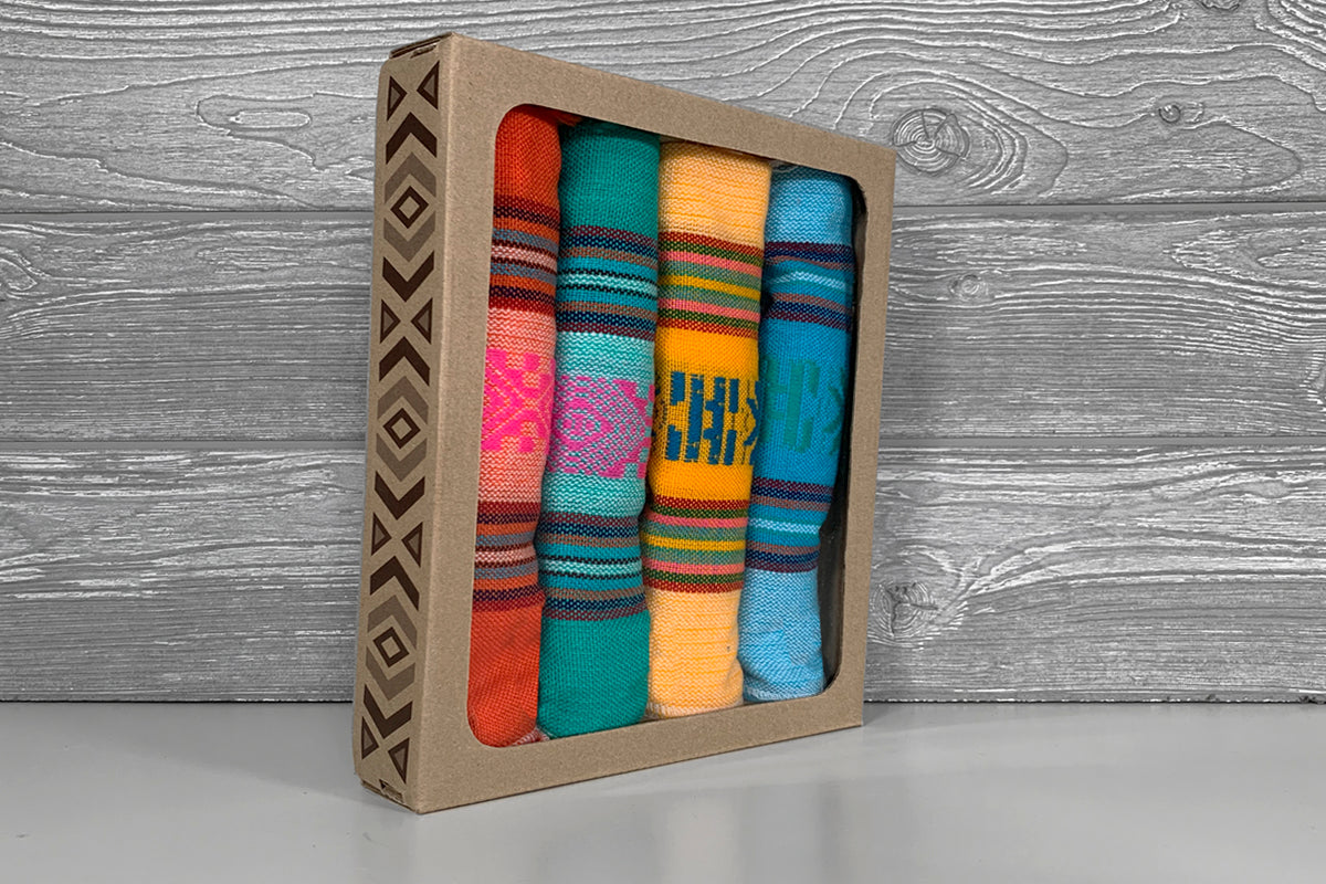 Set of four colorful woven napkins with striped patterns in red, teal, yellow, and blue in kraft box.