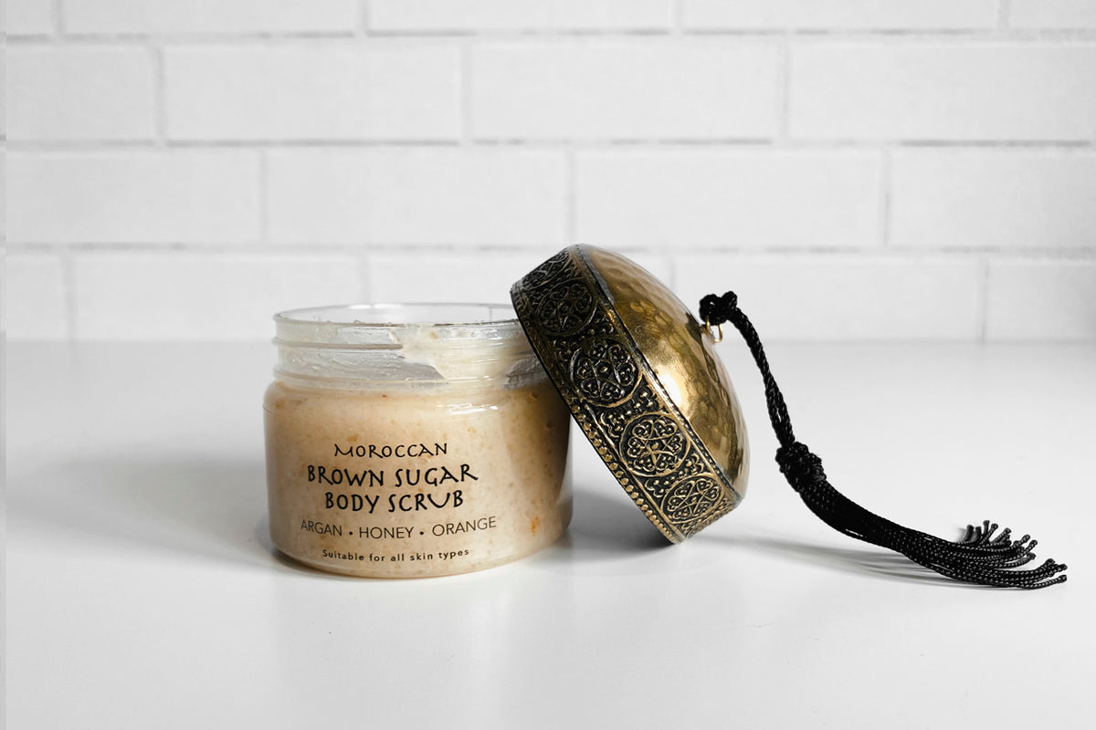 Brown sugar body scrub in glass jar with ornate brass lid and black tassel next to it.