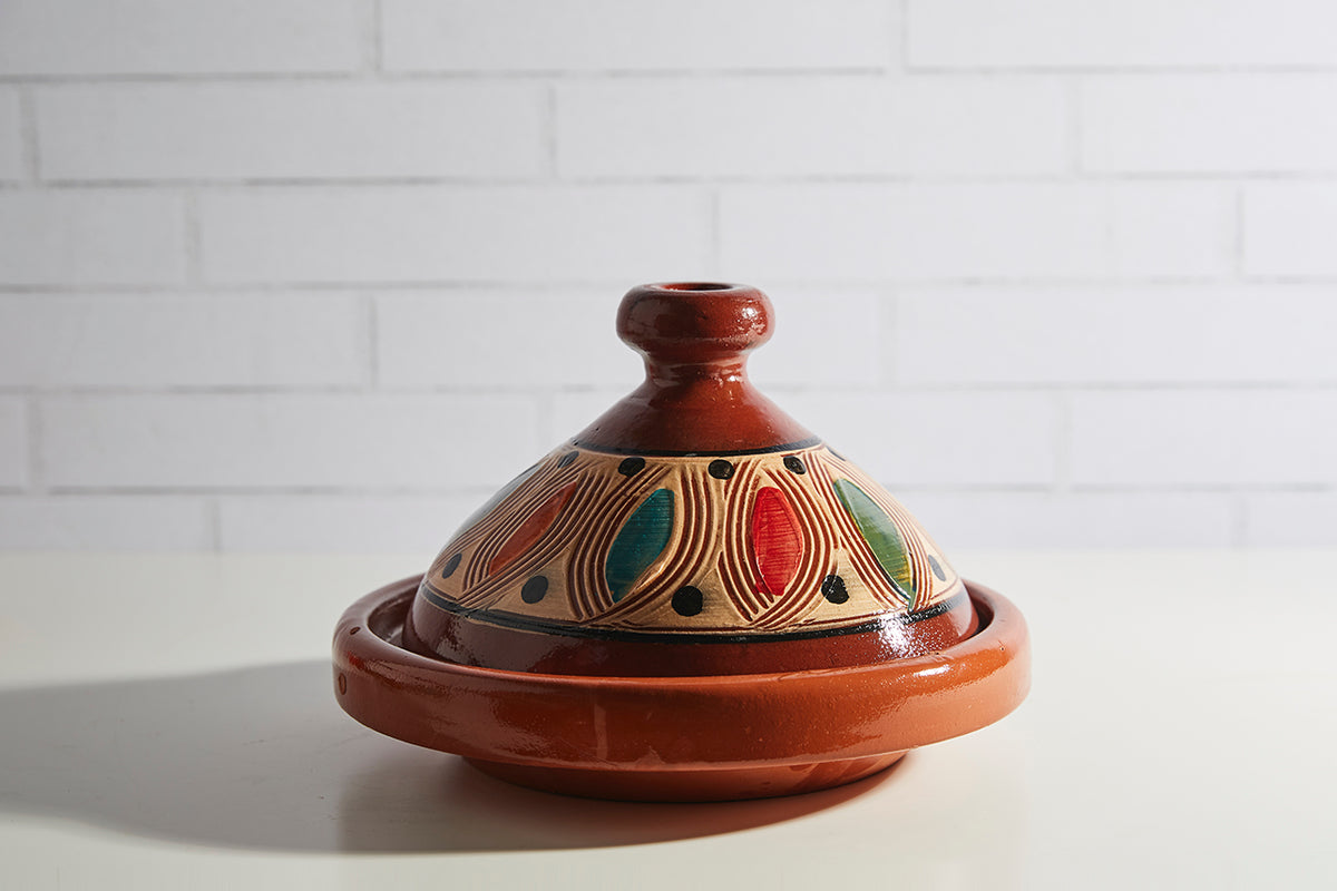 Terracotta tagine with conical lid featuring geometric patterns in gold, red, teal, and black.