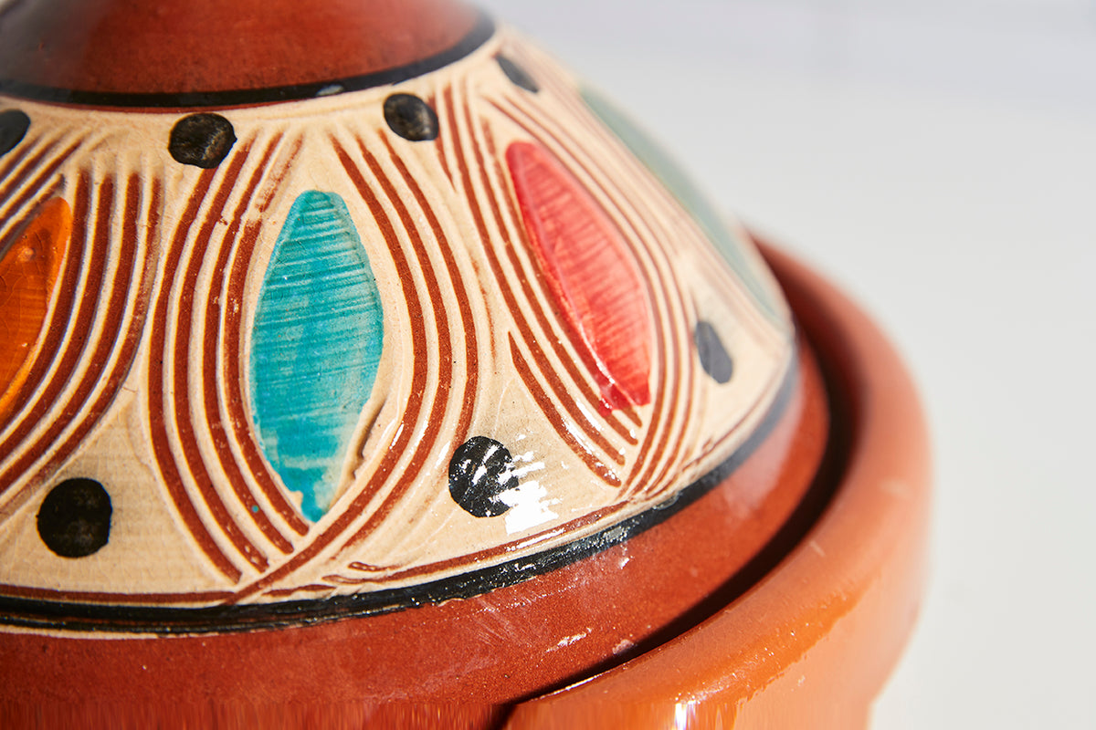 Terracotta tagine with conical lid featuring hand-painted geometric patterns in red, blue, and black.