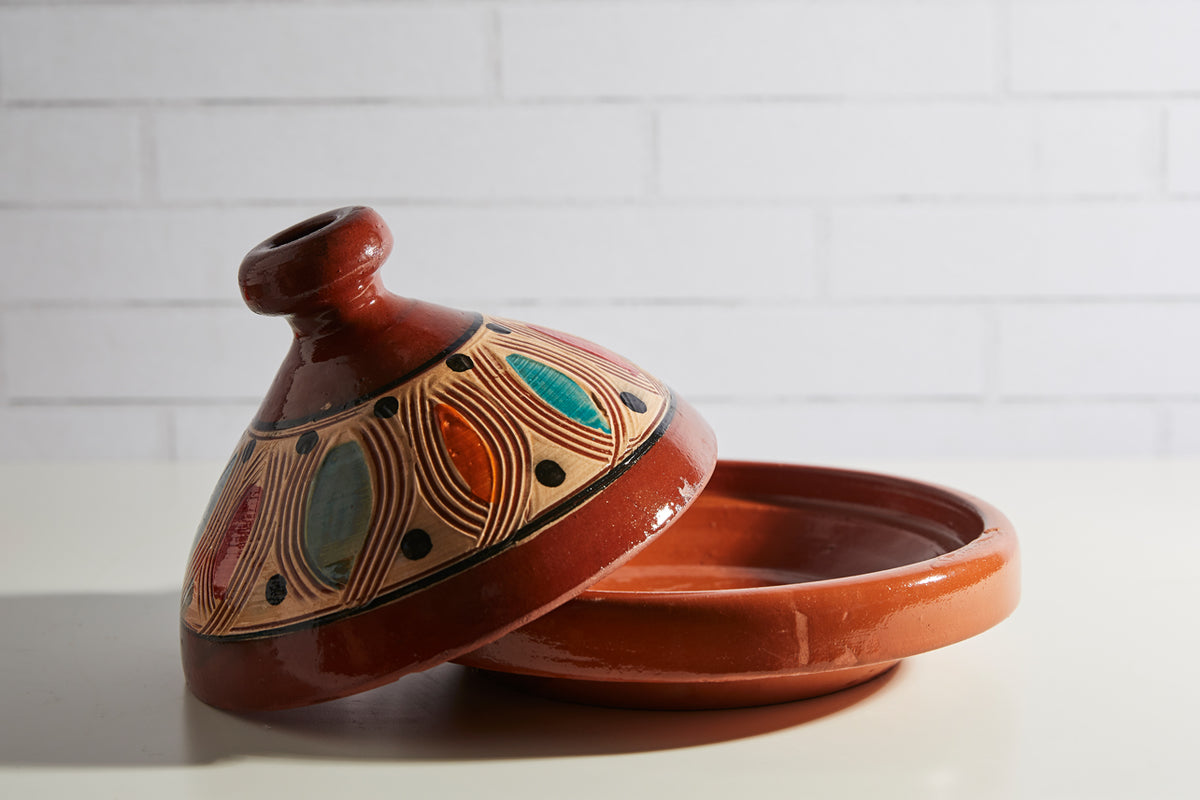 Terracotta tagine with conical lid featuring geometric patterns in teal, gold, and black with a rounded knob finial.