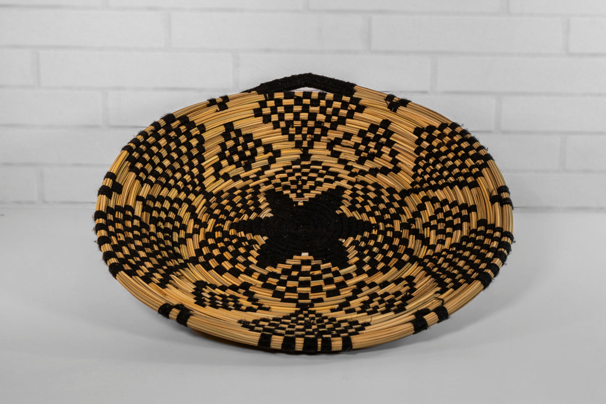 Woven tray with natural tan and black geometric pattern, shallow curved bowl shape.