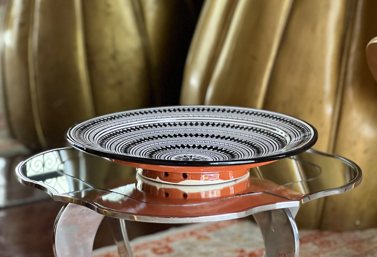 Ceramic couscous platter with geometric black and white pattern on rim, terracotta base, and metal handles.