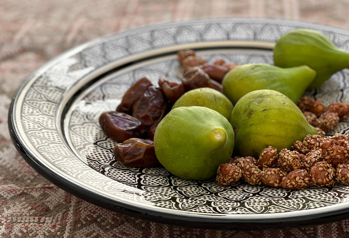 Decorative ceramic platter with green pears, dates, and nuts arranged on patterned surface.