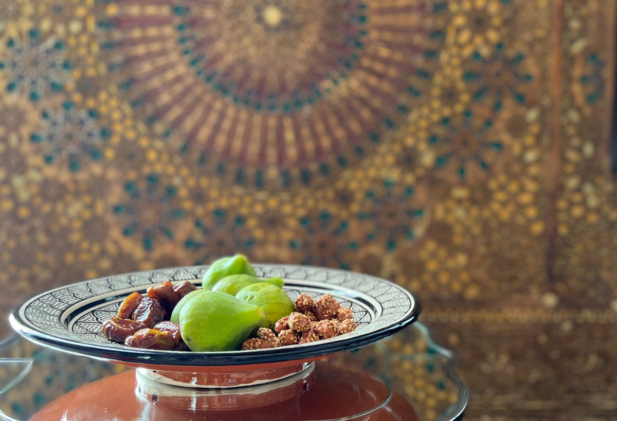Moroccan ceramic platter with decorative geometric patterns holding couscous, green grapes, and dried dates.