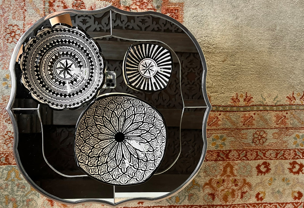 Three white ceramic bowls with black geometric and floral patterns, nested inside a scalloped black serving tray.