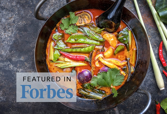Red curry in black wok with green peppers, red chilis, cilantro, and purple onion served with chopsticks.