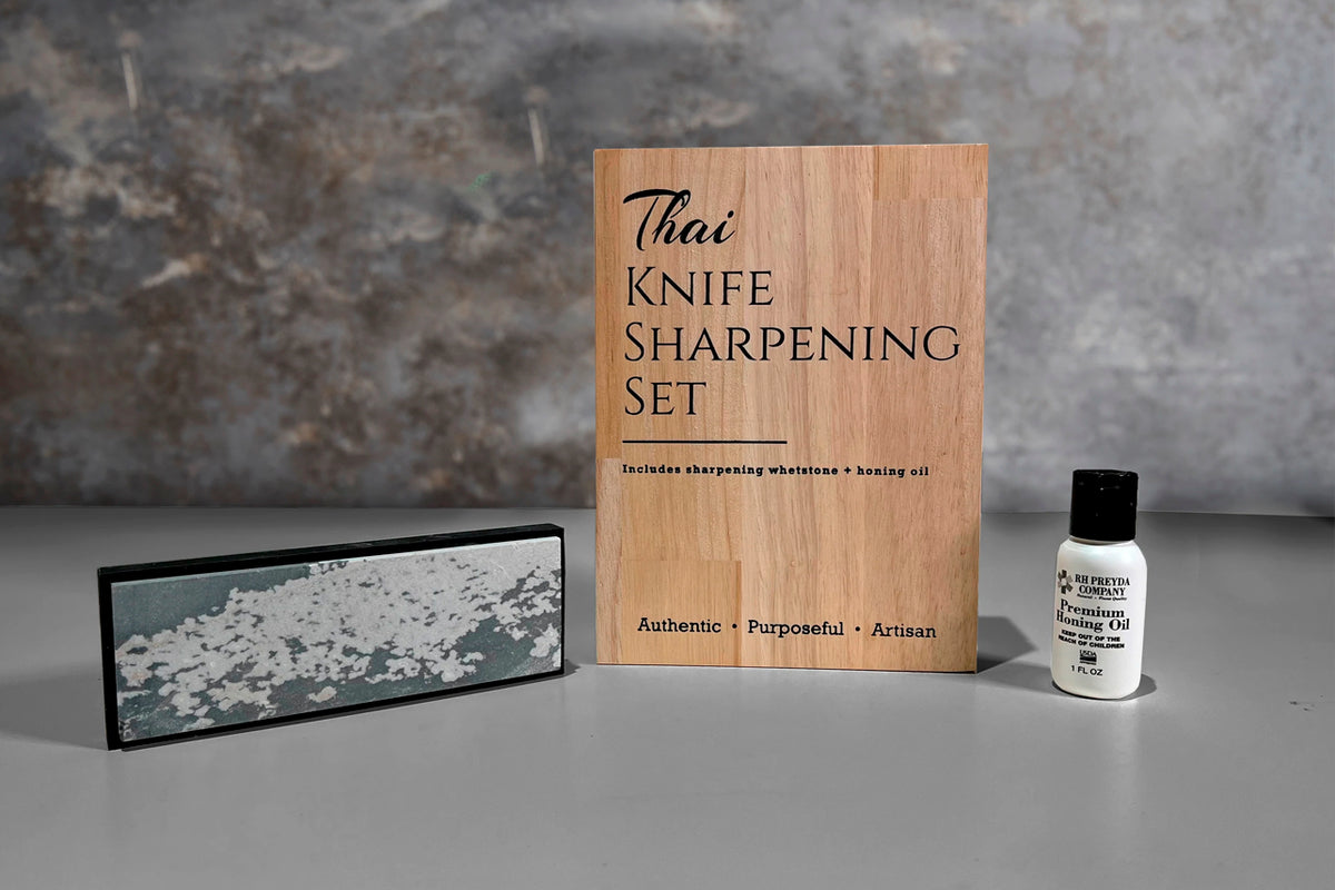 Thai knife sharpening set with wooden box, whetstone, and honing oil bottle displayed together.