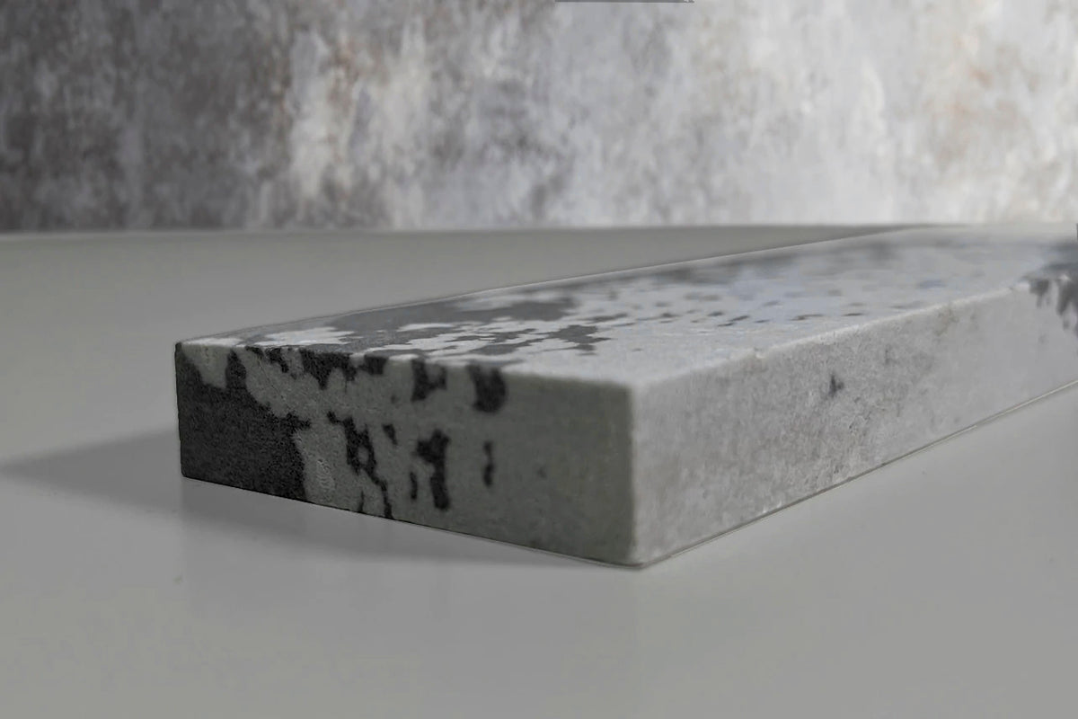 Rectangular whetstone with textured gray and white surface and dark speckled patterns.