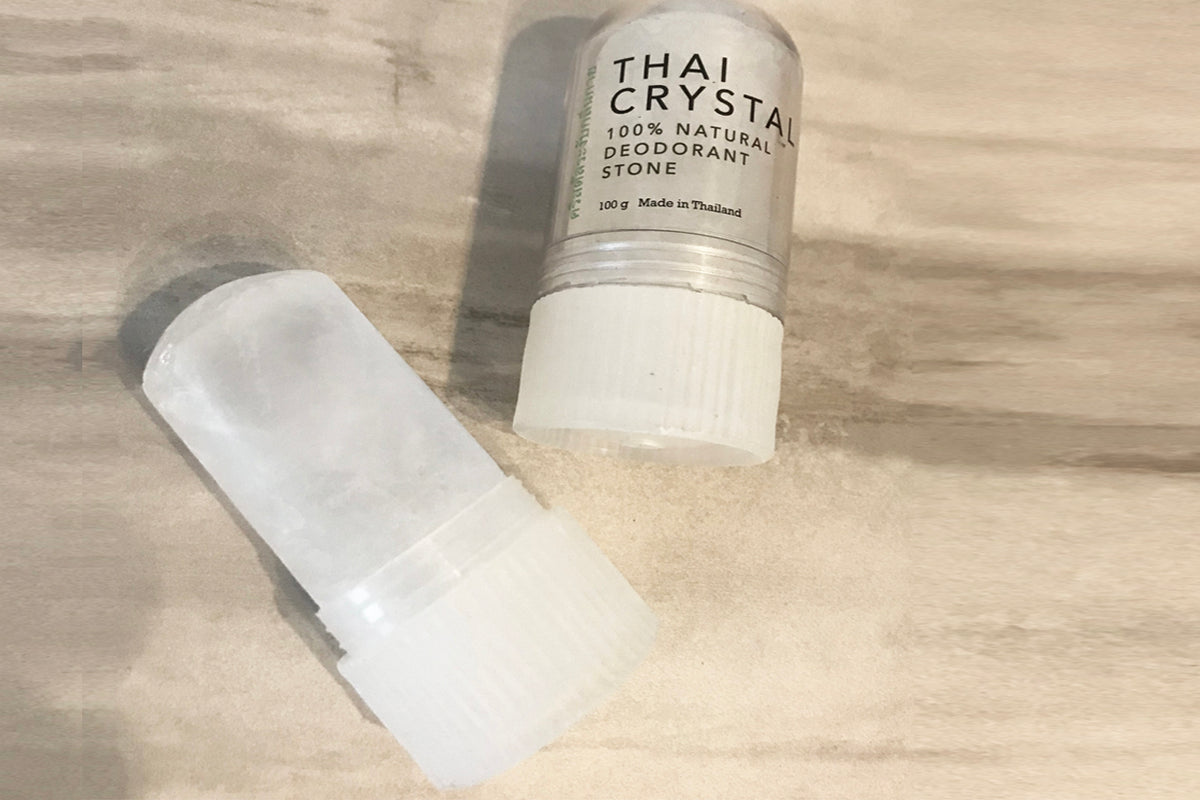 Two white cylindrical Thai crystal deodorant stones with labels and plastic application caps on a light wood surface.