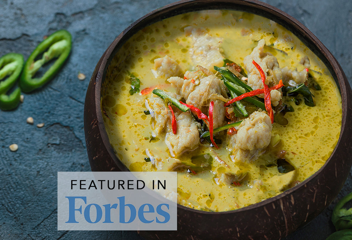 Green curry with chicken, green chilies, and herbs in a dark bowl on blue surface.
