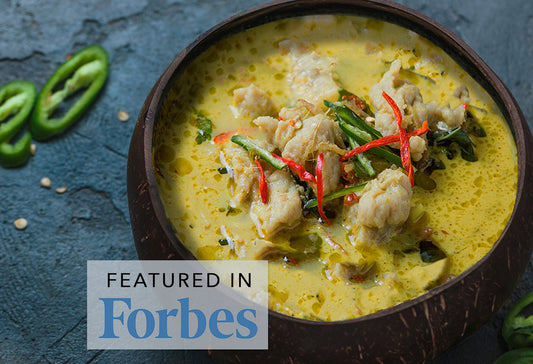Green curry with chicken, green chilies, and herbs in a dark bowl on blue surface.