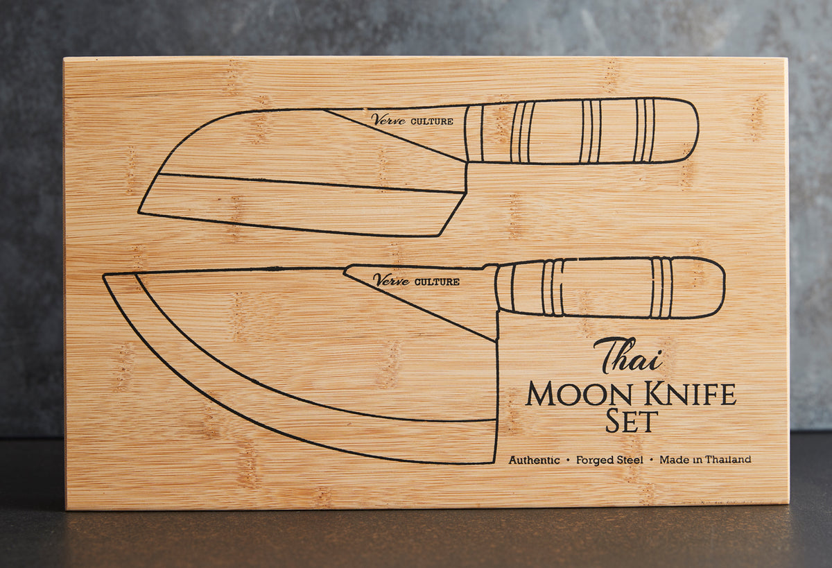 Bamboo cutting board with engraved illustrations of two curved Thai moon knives with wrapped handles and product text.