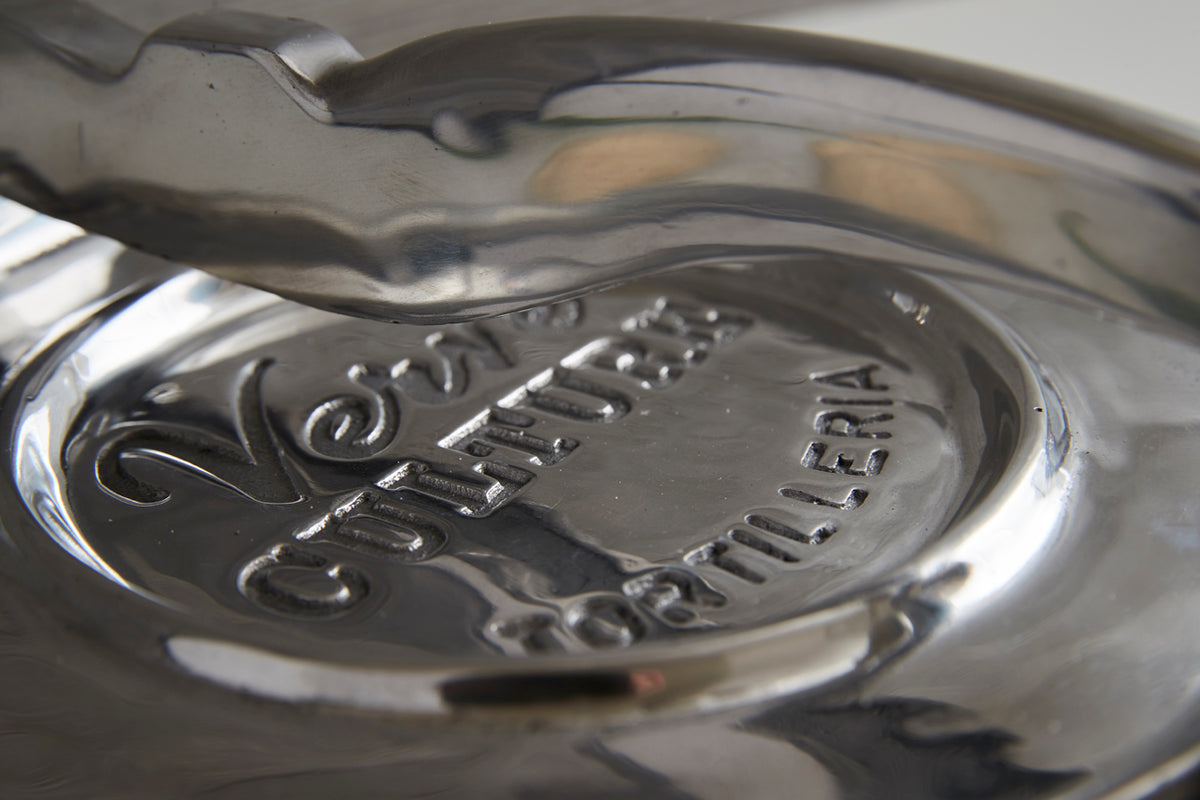 Polished aluminum tortilla press with embossed decorative design on the pressing plate and hinged handle.