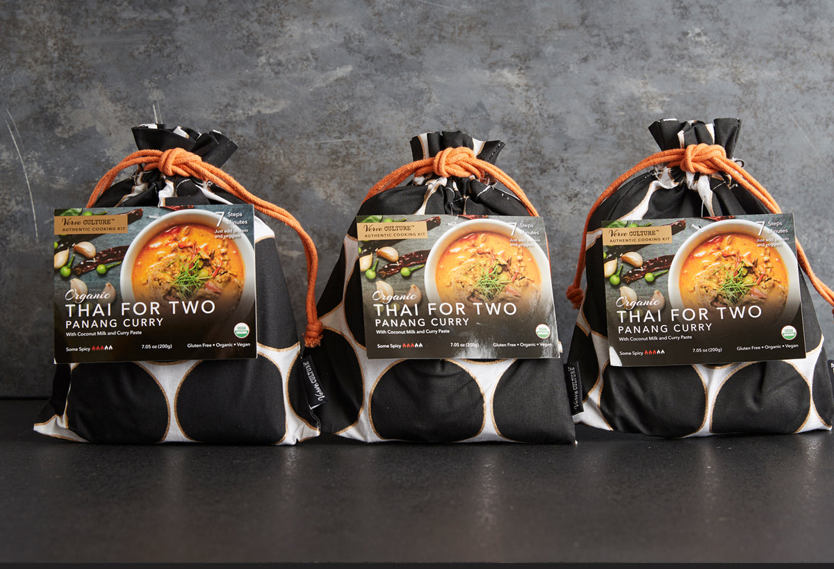 Three black pouches with orange ties containing organic panang curry kits, each displaying a label with a bowl of orange curr
