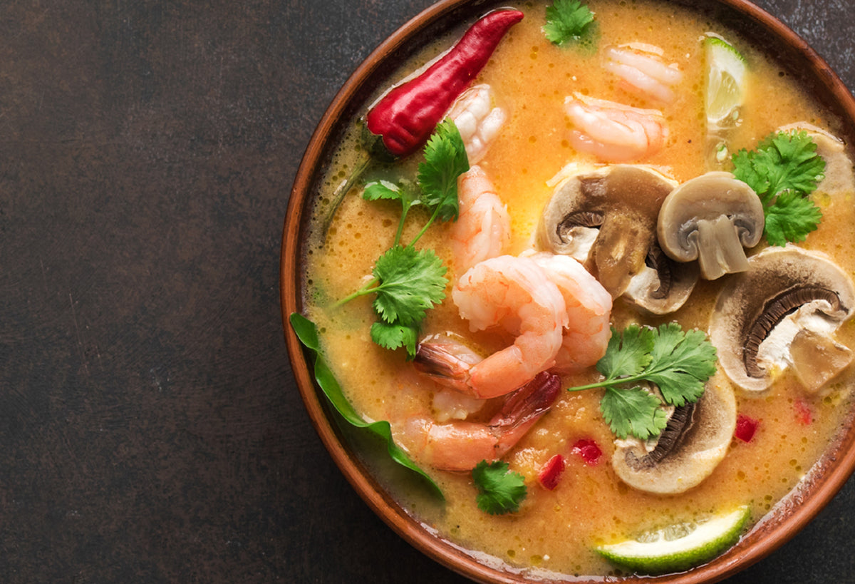 Tom yum soup with shrimp, mushrooms, cilantro, red chili, and lime in clay bowl.