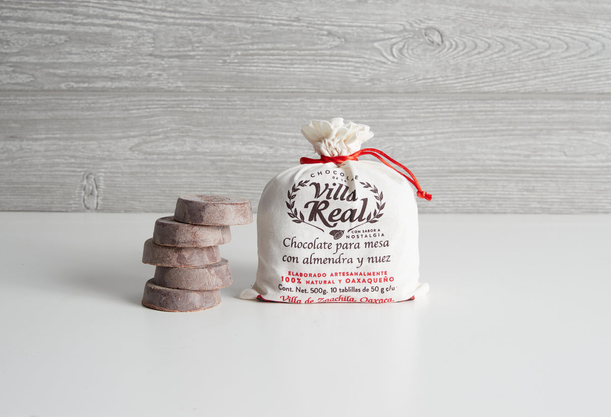 Villa Real Mexican hot chocolate package with red drawstring tied at top, displayed next to stacked chocolate tablets on whit