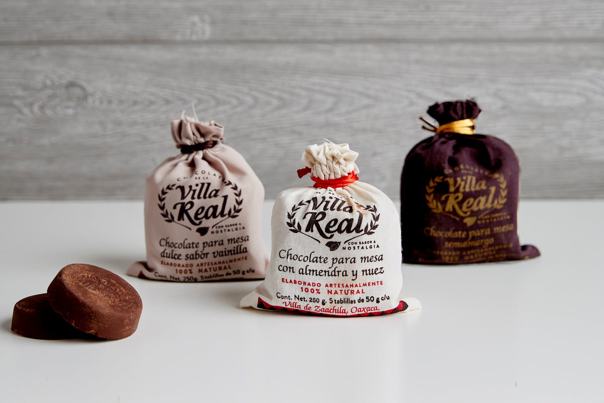 Three Villa Real Mexican hot chocolate packets in cloth bags with a chocolate ball displayed in front.