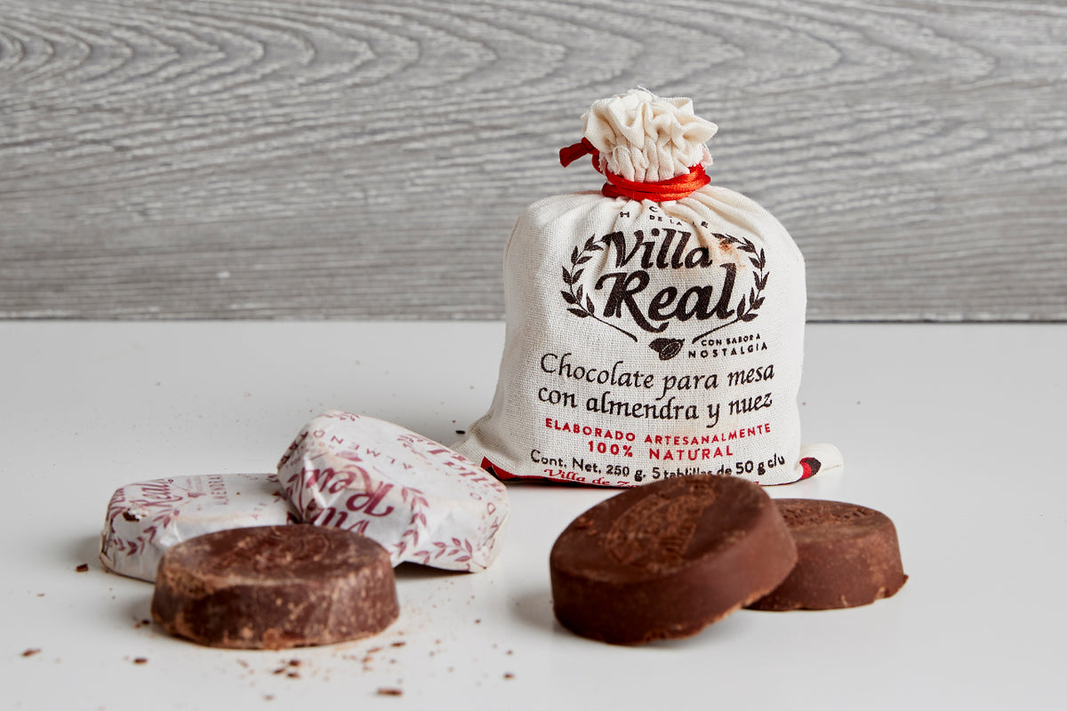 Villa Real Mexican hot chocolate package with wrapped and unwrapped brown chocolate tablets on white surface.