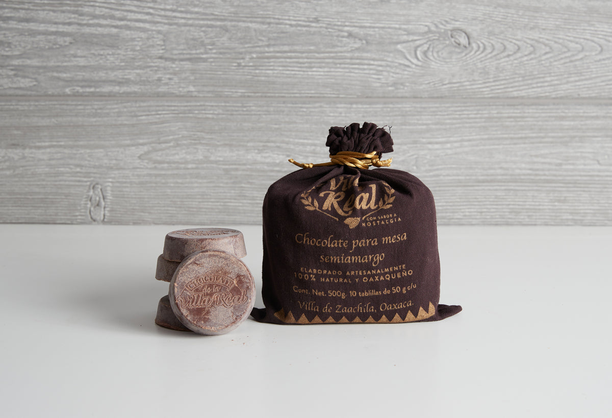 Villa Real Mexican hot chocolate package with black cloth wrapping and gold text next to unwrapped tablet on white surface.
