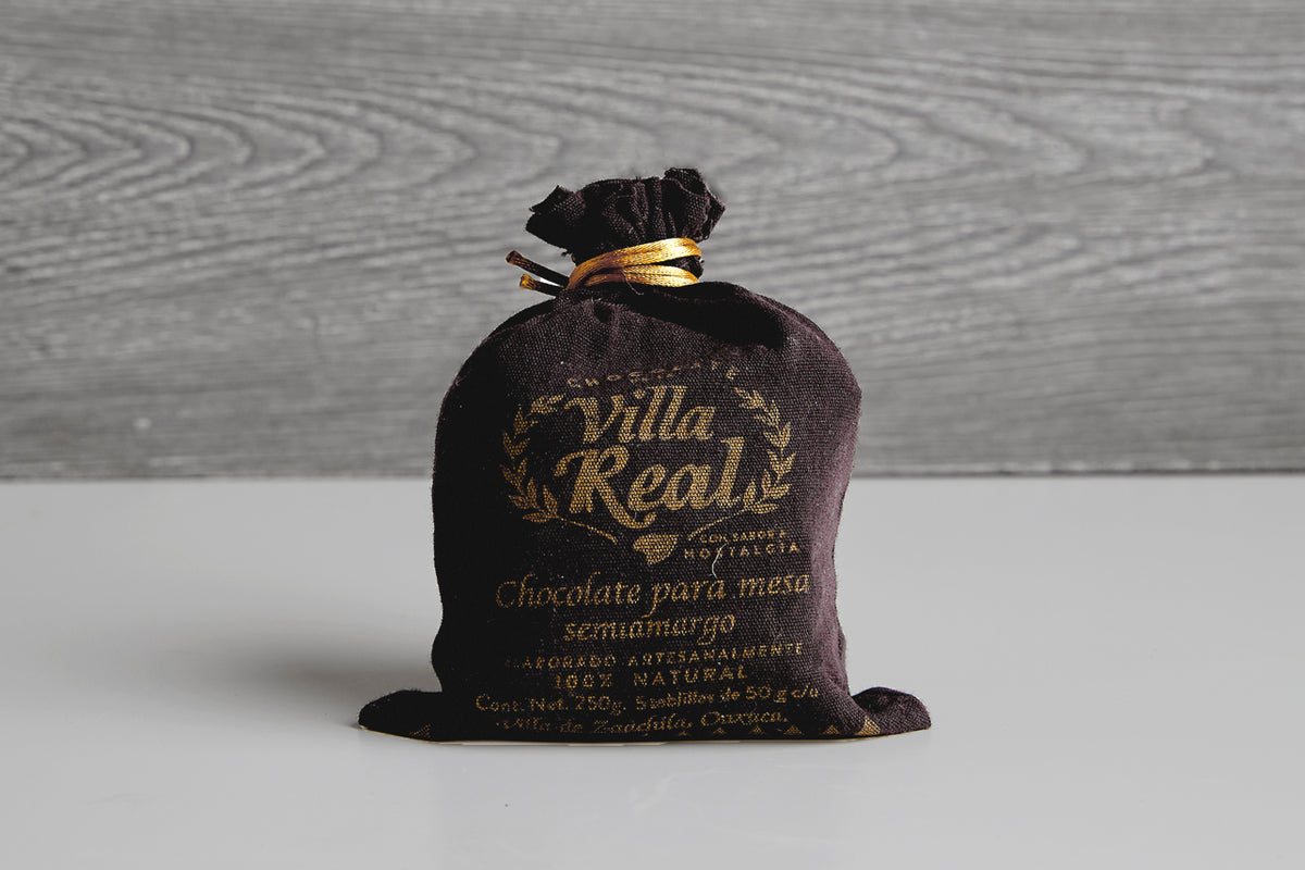 Black cloth pouch with gold text and gold ribbon tie containing Villa Real Mexican hot chocolate mix.