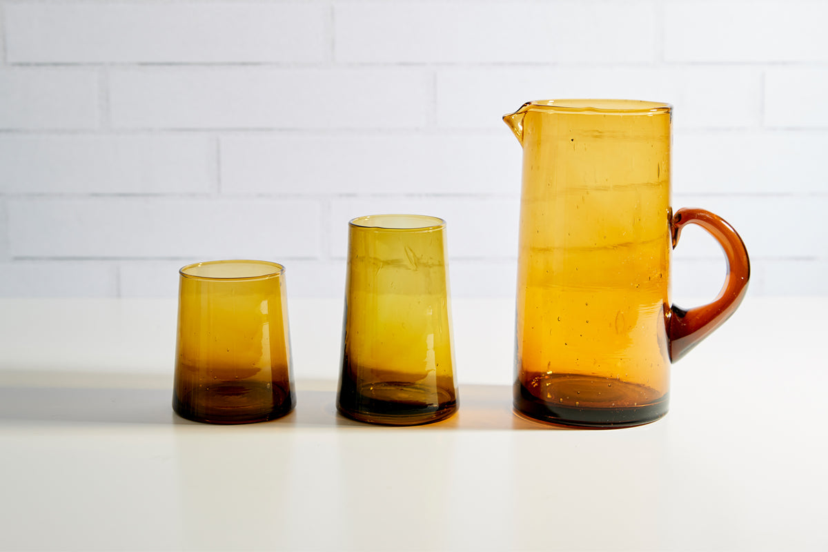 Three amber cone-shaped glasses and a matching pitcher with amber handle displayed in graduated sizes.