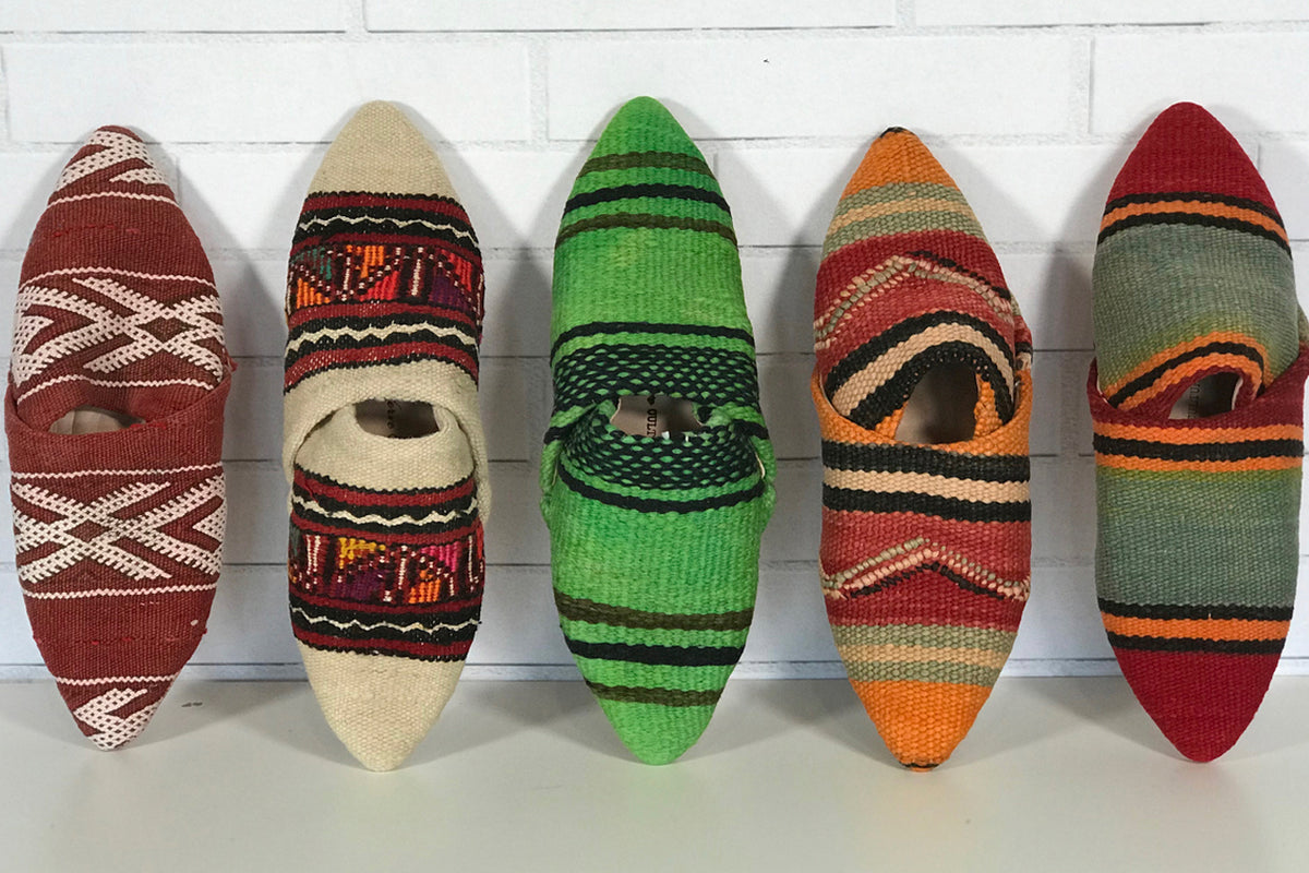 Five knitted slippers in geometric patterns featuring burgundy, cream, green, orange, and red colorways with striped and wove