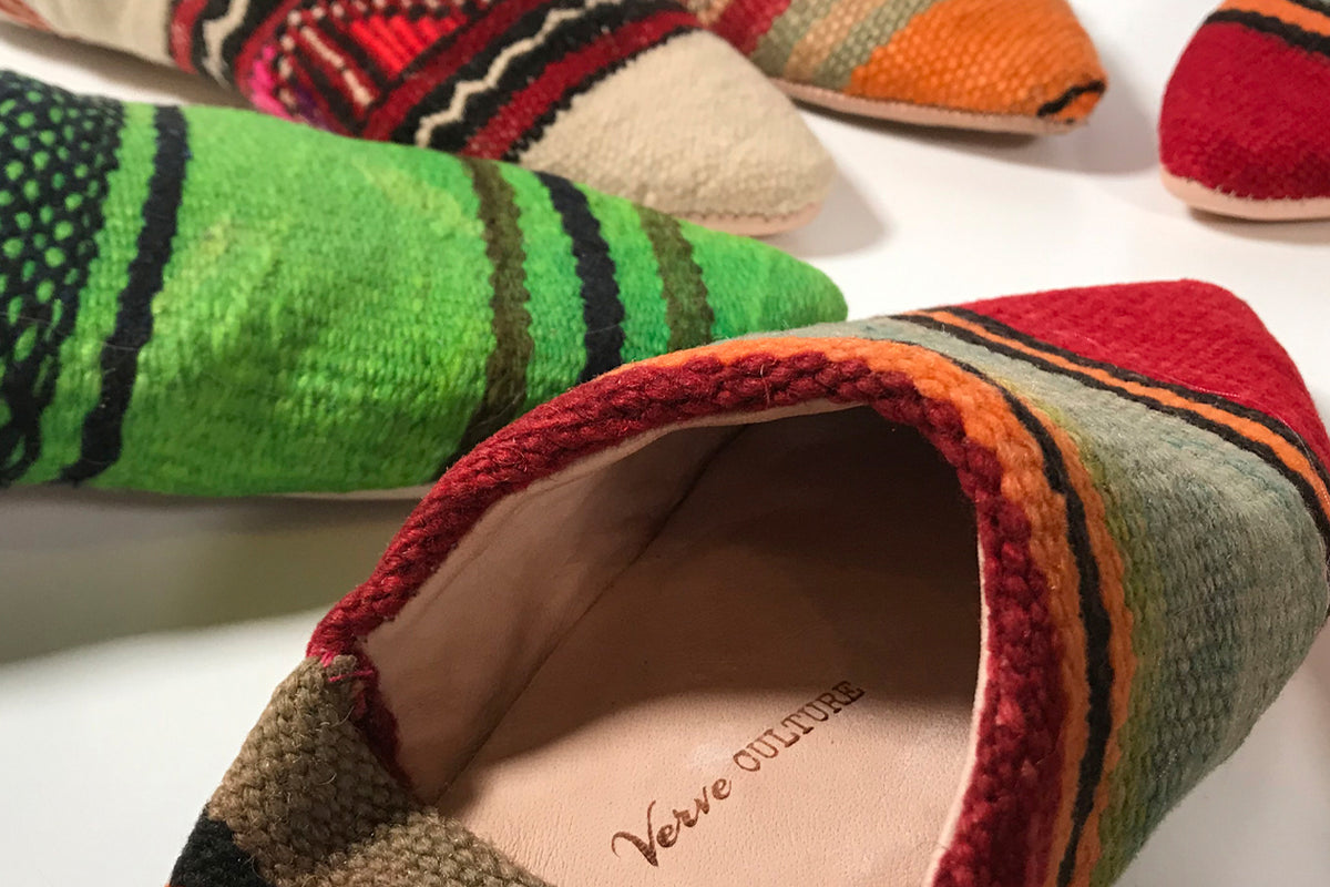 Colorful kilim slippers with geometric patterns in red, green, orange, and neutral tones, showing interior lining detail.