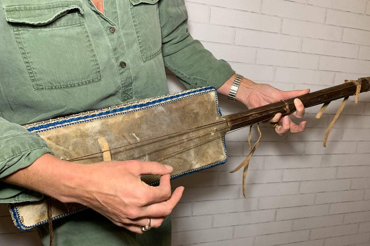 Gimbri with wooden body, leather resonance chamber, and string details, held by person wearing green shirt.