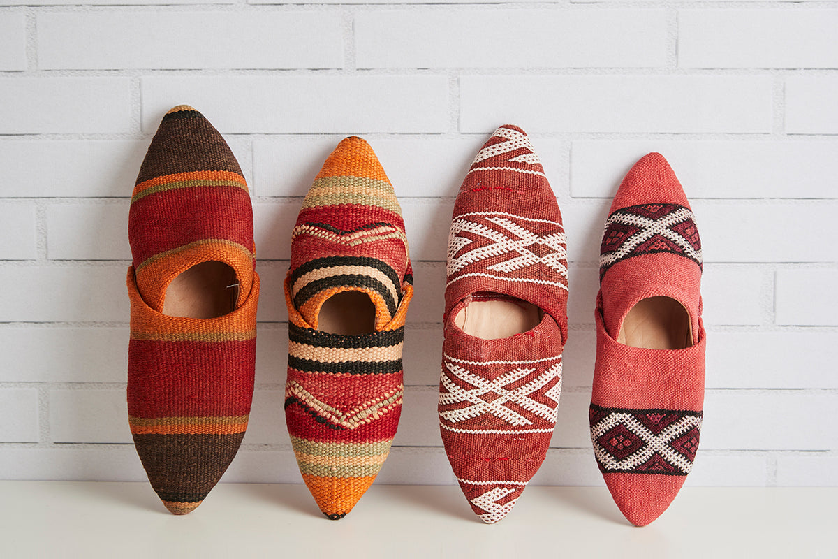 Four Moroccan kilim slippers with geometric patterns in red, orange, brown, and cream colors.
